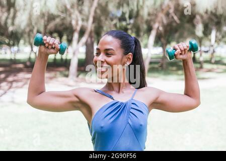 Atleta femminile con pesi a mano che praticano al parco pubblico Foto Stock