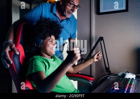 Ragazzo allegro festeggia la vittoria con nonno mentre gioca a videogame a casa Foto Stock