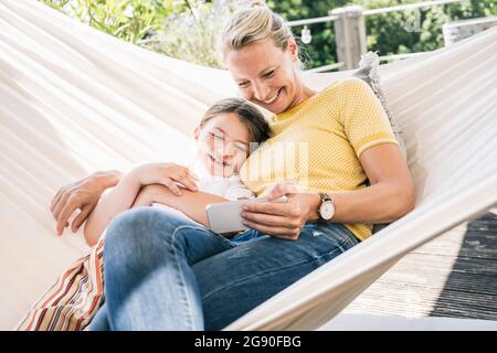 Madre e figlia sorridono mentre si rilassano sull'amaca sul balcone Foto Stock