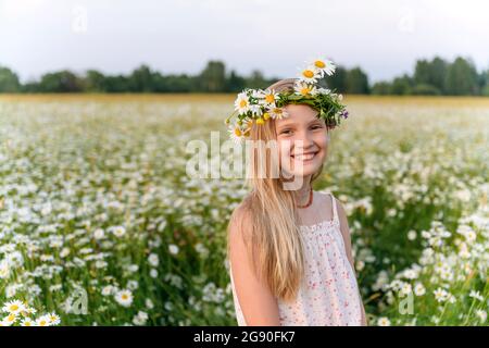 Ragazza con tiara camomilla sorridente in piedi in campo Foto Stock