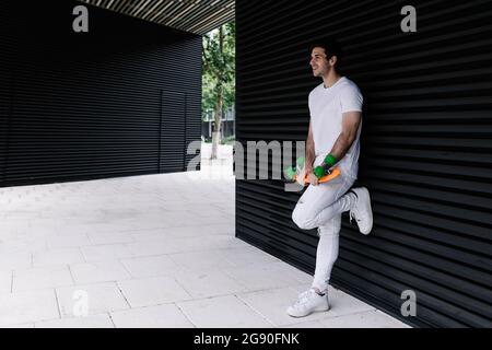 Giovane uomo con skateboard appoggiato sull'otturatore Foto Stock