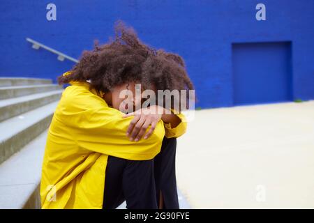 Donna triste fissando mentre abbraccia le ginocchia sui gradini Foto Stock