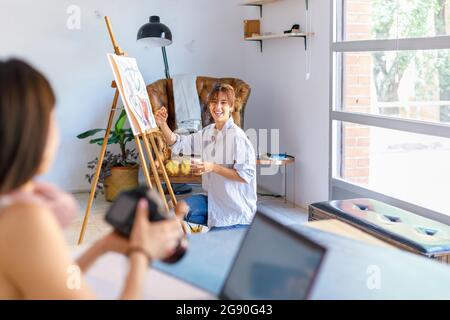 Pittrice sorridente che guarda il fotografo collega che tiene la fotocamera in studio Foto Stock