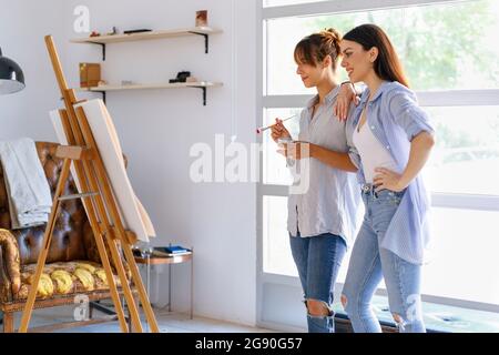 Artisti femminili che guardano la pittura mentre si levano in piedi insieme nello studio d'arte Foto Stock