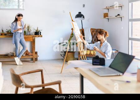 Artista femminile che dipinge mentre fotografo collega che ascolta musica in studio Foto Stock
