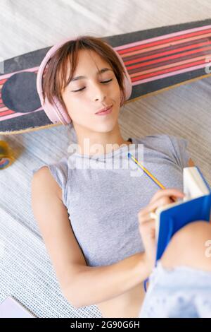 Giovane artista femminile che scrive in blocco note mentre si trova sullo skateboard in studio Foto Stock