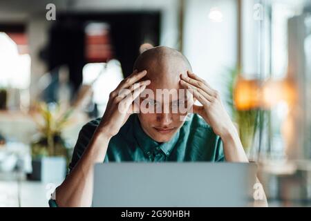 Un giovane uomo d'affari preoccupato con la testa nelle mani che guarda il laptop in un caffè Foto Stock