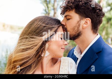 Uomo affettuoso con gli occhi chiuso baciare la ragazza sulla fronte Foto Stock