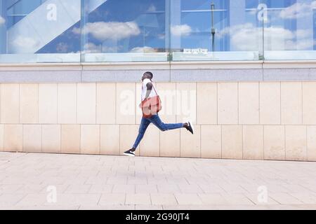 Giovane uomo con borsa a spalla che corre a parete Foto Stock