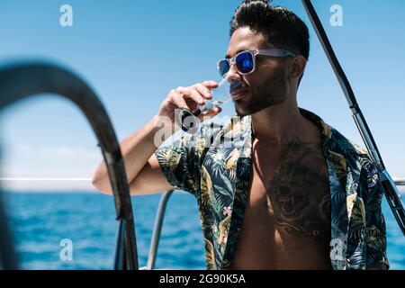 Giovane uomo che guarda via mentre beve in yacht durante la vacanza Foto Stock