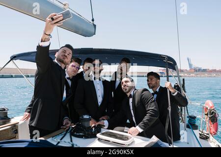 Uomo che prende selfie con gli amici di sesso maschile attraverso il telefono cellulare in yacht Foto Stock