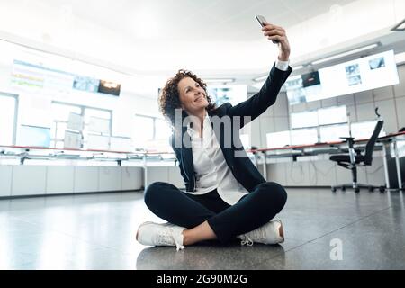Donna d'affari sorridente che prende selfie attraverso il telefono cellulare alla sede centrale Foto Stock
