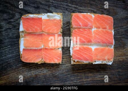 Due tostature di pane a grani interi con formaggio cremoso e salmone leggermente salato su un pannello di legno scuro. Disposizione piatta. Spazio di copia. Concetto, colazione sana, foo Foto Stock