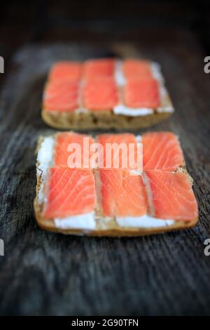 Due tostature di pane a grani interi con formaggio cremoso e salmone leggermente salato su un pannello di legno scuro. Disposizione piatta. Spazio di copia. Concetto, colazione sana, foo Foto Stock