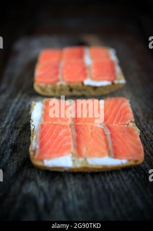 Due tostature di pane a grani interi con formaggio cremoso e salmone leggermente salato su un pannello di legno scuro. Disposizione piatta. Spazio di copia. Concetto, colazione sana, foo Foto Stock