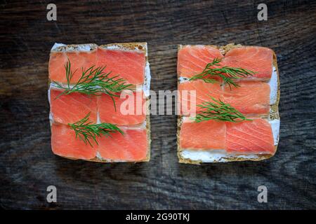 Due toast di pane a grani interi con formaggio cremoso e salmone leggermente salato e aneto su una tavola di legno scuro. Disposizione piatta. Spazio di copia. Concetto, pausa sana Foto Stock