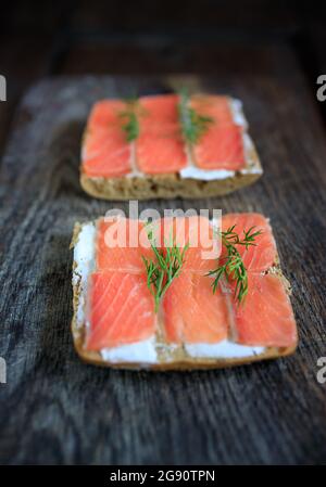 Due toast di pane a grani interi con formaggio cremoso e salmone leggermente salato e aneto su una tavola di legno scuro. Disposizione piatta. Spazio di copia. Concetto, pausa sana Foto Stock