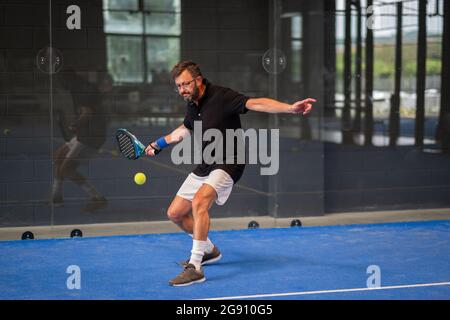 Uomo che gioca a un padel in un campo di erba blu al coperto - giovane sportivo ragazzo padel giocatore che colpisce palla con una racchetta Foto Stock