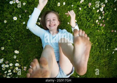 La ragazza si trova sull'erba con le braccia e le gambe sollevate. Foto Stock