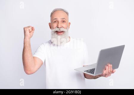 Foto di felice attraente vecchio uomo raise pugno vincitore tenere computer isolato su sfondo grigio Foto Stock