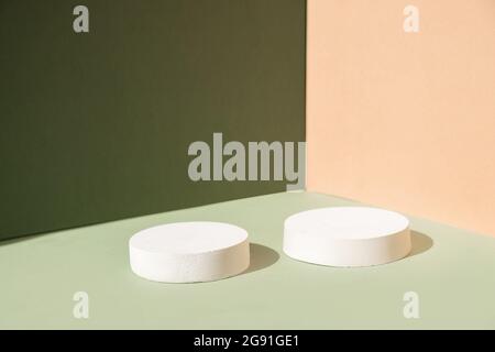 Scena minima astratta con forme geometriche. Podi cilindrici su sfondo verde e beige. Sfondo astratto. Scenografia per mostrare i podrotti cosmetici Foto Stock