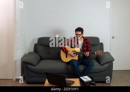 L'uomo latino suona la chitarra davanti al notebook. Foto Stock