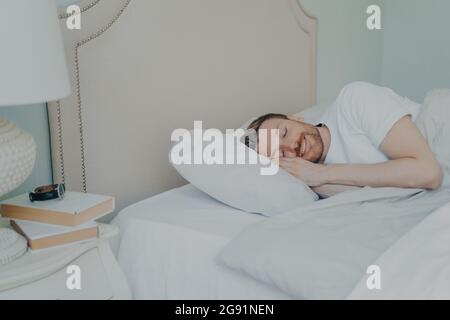 Uomo giovane e rilassato che giace a letto con occhi chiusi Foto Stock
