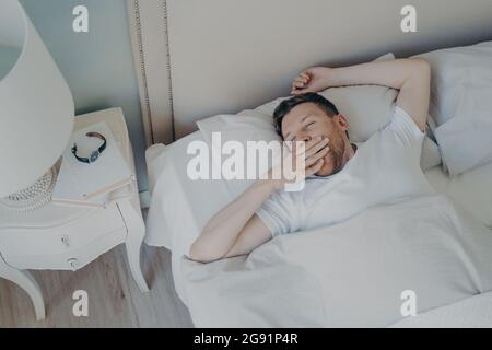 Allegro giovane attraente uomo che si sveglia al mattino a letto Foto Stock