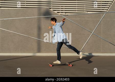 Giovane uomo a bordo di un longboard in città strada skatepark. Il ragazzo hipster casual indossa lo skateboard bandana Foto Stock