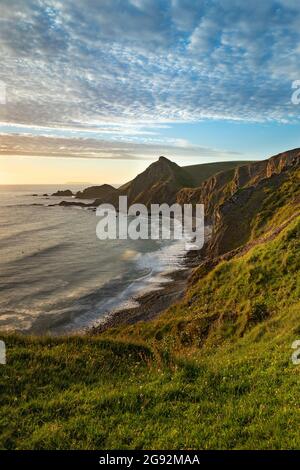 La bassa luce del sole cattura il Tor di Santa Caterina sulla costa nord del Devon. Hartland Quay con vista a distanza di Lundy Island Foto Stock