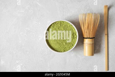Set da tè verde Matcha. Matcha polvere e accessori di bambù per la cerimonia del tè su sfondo grigio. Spazio di copia, vista dall'alto, disposizione piatta. Foto Stock