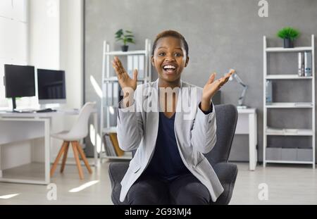 Ritratto di felice donna d'affari seduta sulla sedia da ufficio, aggrappando le mani e sorridendo Foto Stock