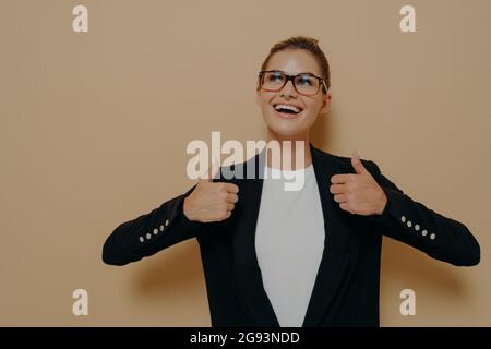 Cliente femminile positivo in occhiali con ampio sorriso che mostra pollici con entrambe le mani Foto Stock