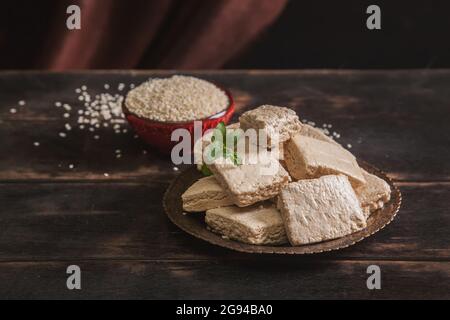 Pezzi di tahini halva, semi di sesamo in una ciotola. Ancora vita in stile orientale su vecchio sfondo di legno marrone Foto Stock