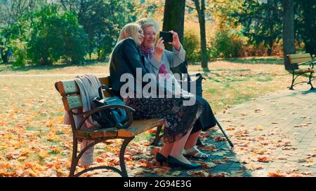 Zoom di giovane donna e sua nonna guardando qualcosa sullo smartphone nel parco. C'è una bella giornata d'autunno soleggiata. Foto Stock