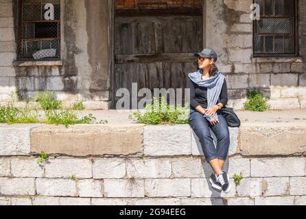 Donna seduta di fronte alla casa di oggetti abbandonati a Rovigno Foto Stock