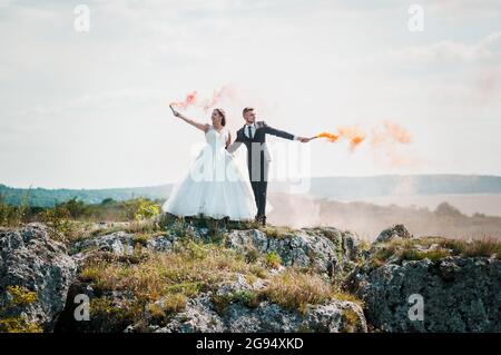 Gli sposi si levano in piedi su una roccia e tengono il fumo arancione colorato nelle loro mani Foto Stock