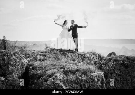 Gli sposi si levano in piedi su una roccia e tengono il fumo arancione colorato nelle loro mani Foto Stock