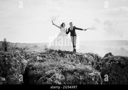 Gli sposi si levano in piedi su una roccia e tengono il fumo arancione colorato nelle loro mani Foto Stock