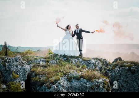 Gli sposi si levano in piedi su una roccia e tengono il fumo arancione colorato nelle loro mani Foto Stock