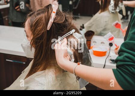 Tintura dei capelli durante il periodo di quarantena, cliente e parrucchiere in maschere, decolorazione dei capelli. Novità Foto Stock