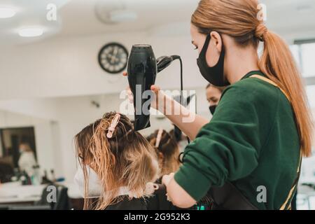 Lo stylist usa un asciugacapelli per modellare i capelli dopo la colorazione. Nuovo Foto Stock