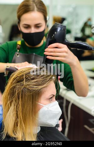 Lo stylist usa un asciugacapelli per modellare i capelli dopo la colorazione. Nuovo Foto Stock