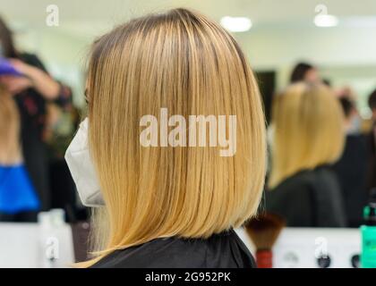 Il parrucchiere femminile tiene a portata di mano tra le dita capelli biondi, pettine e forbici da vicino, raddrizzando le punte dei capelli. Novità Foto Stock
