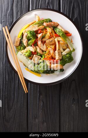 Asian Stir friggere pepe, pak choi, carote, broccoli, pollo e tofu primo piano in un piatto sul tavolo. Vista dall'alto verticale Foto Stock