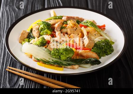 Mescolare la miscela asiatica fritta di pollo, tofu e verdure di stagione in un piatto su fondo di legno nero. Orizzontale Foto Stock