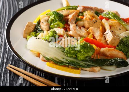 Mescolare il pollo fritto, il tofu, i peperoni, le carote, i broccoli e la ciotola da vicino in un piatto sul tavolo. Orizzontale Foto Stock