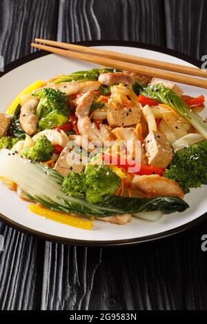 Asian Stir friggere pepe, pak choi, carote, broccoli, pollo e tofu primo piano in un piatto sul tavolo. Verticale Foto Stock