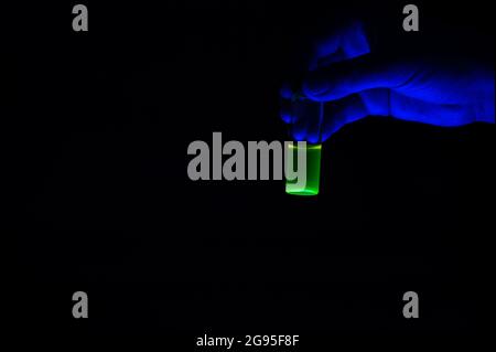 Una donna chimica riassicuratrice che contiene una soluzione di composto fluorescente verde in un piccolo flaconcino di vetro per la ricerca medica Foto Stock