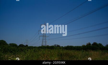 Una vista paesaggistica di tralicci elettrici contro un cielo estivo blu profondo in un ambiente di campagna con spazio di copia. Foto Stock
